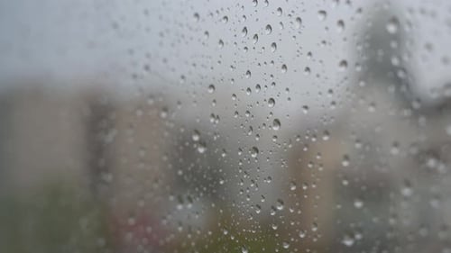 Des gouttes de pluie sur une fenêtre donnant sur un temps maussade et couvert.