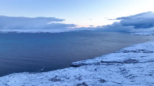Wide aerial view of the cold arctic sea meeting a snowy coastline