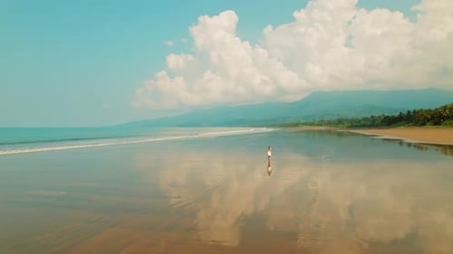 Young woman walks toward the horizon on wide smooth sand beach in Costa Rica