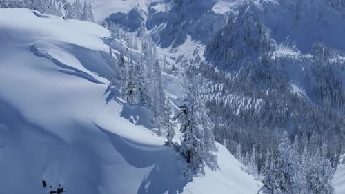 A rotating aerial shot of cliffside revealing a snow covered valley.