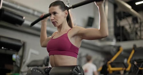 A Young Beautiful Brunette Girl in Sportswear is Exercising on a Machine in the Gym Doing Exercises