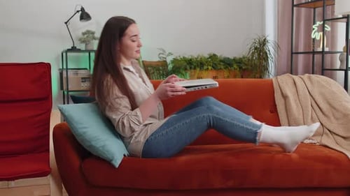 Woman Relaxes on Couch, Opens Laptop, and Smiles