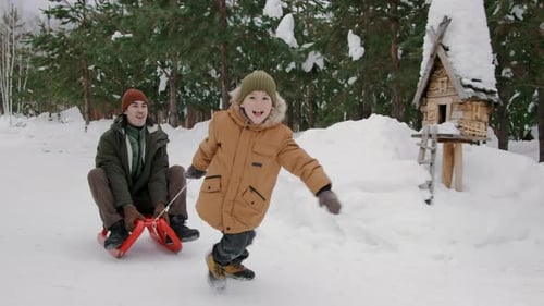 Happy Young Boy Pulling Laughing Father on Sled in Snowy Forest