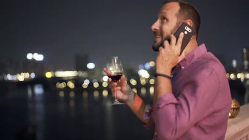 Young Man Talking on Cellphone and Drinking Wine on Terrace in Bar