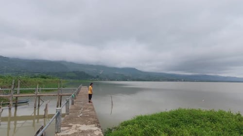 Man Walking on Pier Overlooking Lake and Mountains