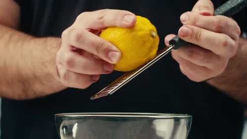 Makro-Nahaufnahme eines professionellen Kochs mit Zitrone und Reibe, bei dem Zitronenschale für Limonadensalat gerieben werden