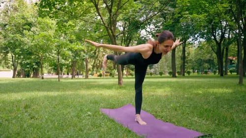 an experienced female instructor meditates in the park practices yoga does stretching on one leg