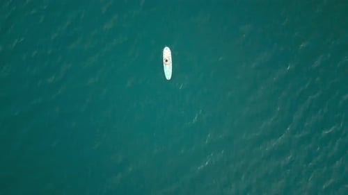 Aerial drone flying over a lake, man doing stand up paddle, with mountains at sunrise. SUP.