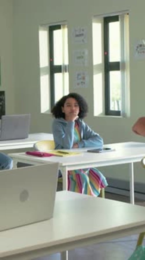 Vertical video: Teacher entering class pointing at laptop, teaching class watching rainbow student