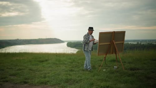 Artist Painting on a Large Canvas in a Tranquil Field By a Lake