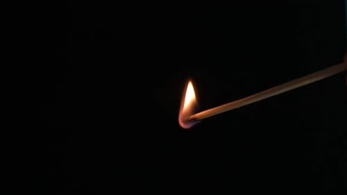Close view of burning match that ignites another match on black background.