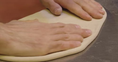 Close up of a pizza chef's hands kneading the dough to prepare a gourmet pizza and spreads the tom