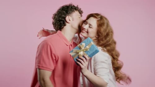 Young American Couple on Pink Studio Background White Man Gives Gift with Bow to Wife or Girlfriend