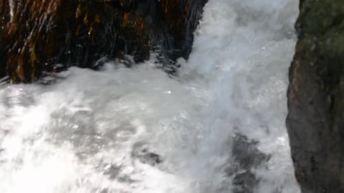 Rapid water splashing in the creek, small yet powerful water stream flowing down fast through rocks.