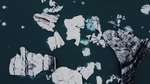 Drohnenaufnahme wunderschöner schwarz-weißer Eisberge, die in einer dunkelblauen Lagune in Island schwimmen