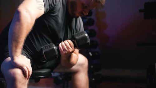 Young active strong man biceps muscle workout training with dumbbell weight in dark gym