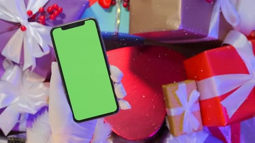 Close-up of hands holding smartphone with chromakey screen against background of gift boxes