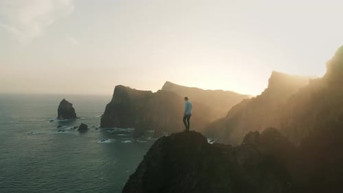 Man Standing on Rocky Cliff Edge at Sunset