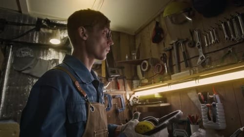 Male Mechanic Putting on Protective Earmuffs and Face Shield in Garage