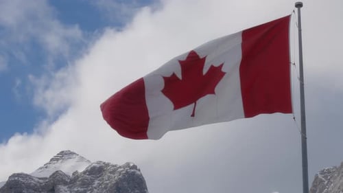 Canadian flag waving in the wind against the blue sky and snowy mountains