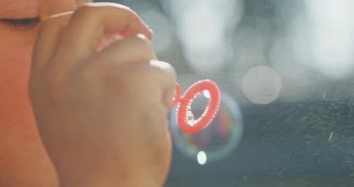 Authentic close up shot of little girl blowing soap bubbles in spring park on a sunny day.