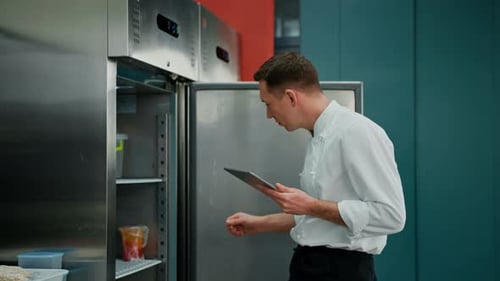 Chef Using Tablet Inspecting Refrigerator in Commercial Kitchen