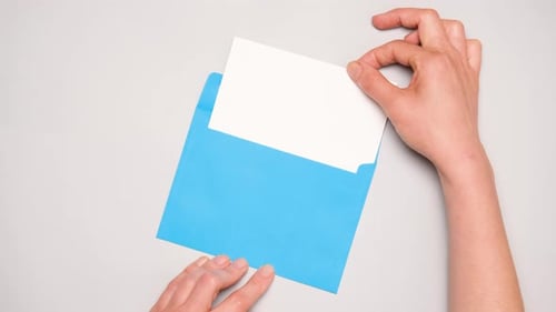 A Hand Pulls Out a White Card From a Bright Blue Envelope Top View of a Blue Envelope on Gray