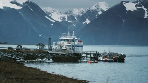 A ferry and other boats docked in the small harbor. Snow-capped mountains in the background.