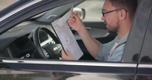 A Sad Angry Man Sits in a Car and Looks at the Bills or Checks Issued to Him