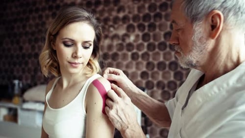 Senior Doctor Applies Kinesiology Tape to Young Woman
