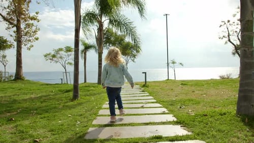 Small Child in Denim Jacket and Jeans Goes Into Distance Along Path Leading to Sea or Endless Ocean