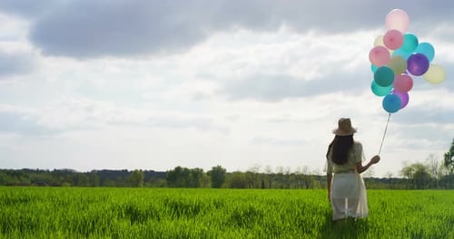 Woman Holding Balloons in a Green Field