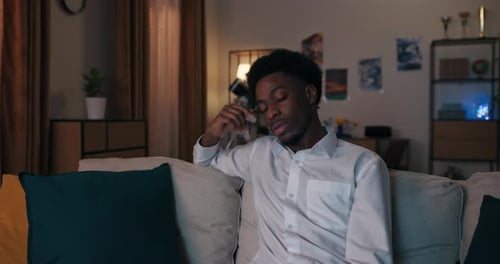 After Hard Day's Work Man of African Appearance in White Shirt is Sitting on Sofa and Tiredly