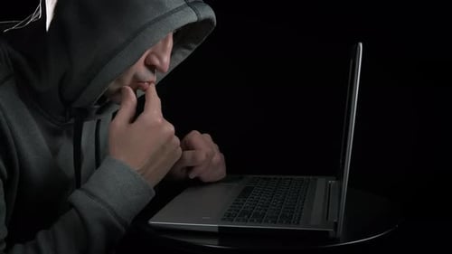 Hooded Figure Typing on Laptop in the Dark