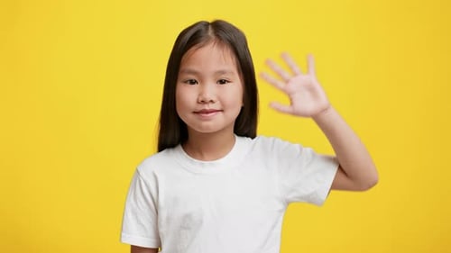 Smiling Child Waves Hello Against a Bright Yellow Background