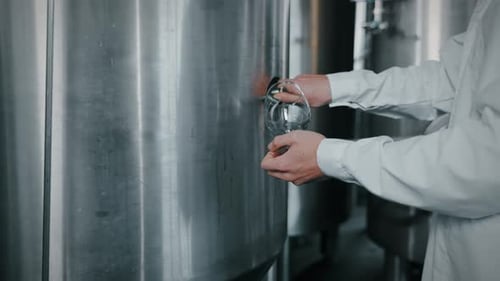 Man in Lab Coat Pours Liquid from Vat