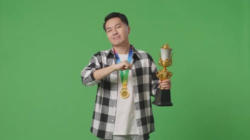 Mann mit Goldmedaille zeigt Goldtrophäe vor die Kamera, lächelt und zeigt auf sich selbst auf den grünen Bildschirm