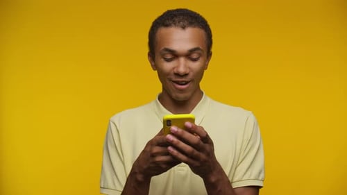 Young Adult Celebrates Smartphone Success on Yellow Background