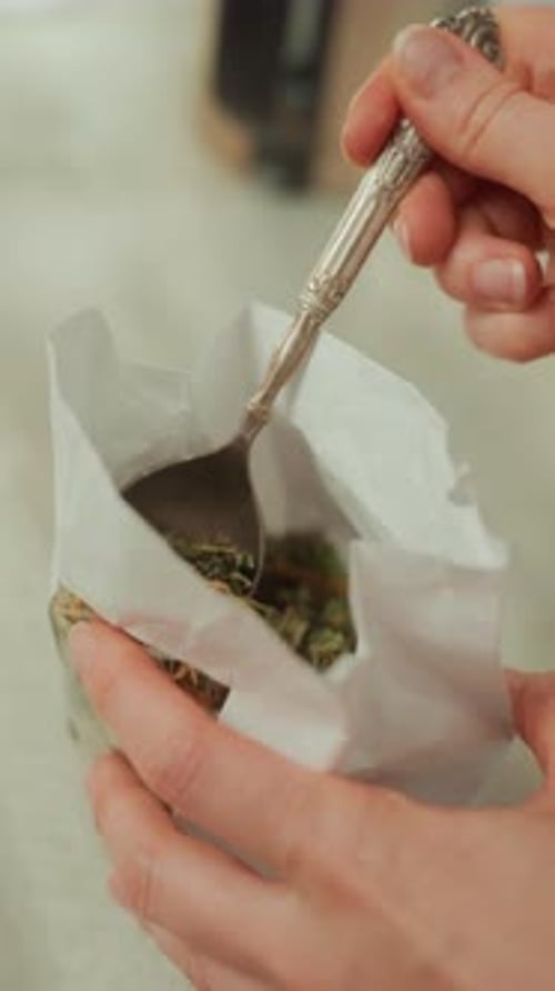 Scooping Herbs into Glass Teapot for Herbal Tea