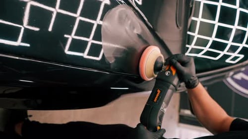 Close-up of a car wash worker using a polishing machine to polish the hood of black luxury car