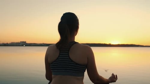 Portrait of a Girl Meditating in the Lotus Position on the Lake at Sunset