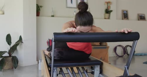 Fit senior caucasian woman stretching on reformer in pilates studio, unaltered, in slow motion