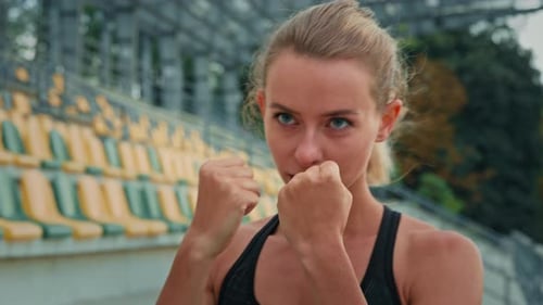 Motivated Female Fighter Athlete with Clenched Fists Standing in Boxing Stance Punching Air Dynamic