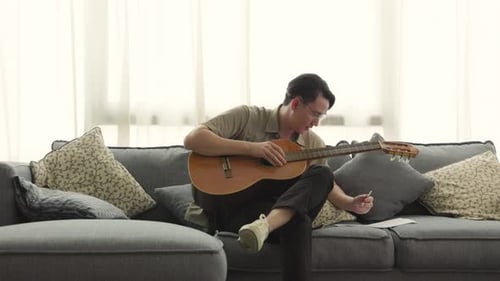 Young Adult Plays Guitar on Couch, Writes Music