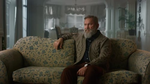 Bearded man sitting contemplatively on sofa in living room