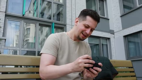 Man Playing Mobile Game on Phone Sitting on Bench