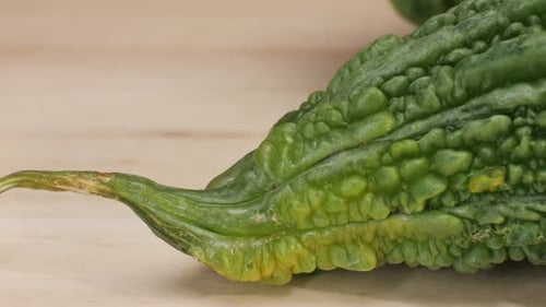 Une gourde amère, un légume souvent utilisé comme ingrédient en cuisine, est posée sur une table en bois.