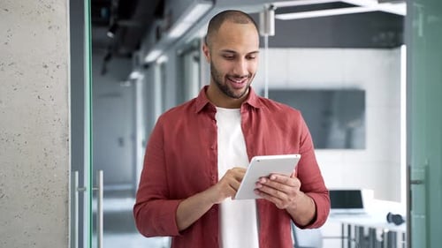 Smiling businessman is using digital tablet while standing in a modern business office.