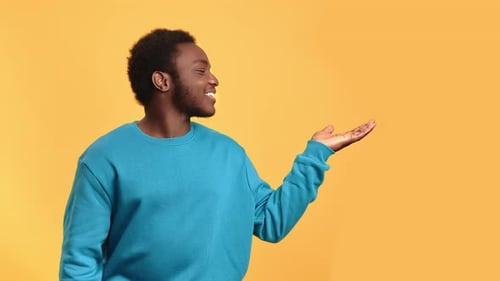Smiling Young Man Presents with Open Palm on Yellow