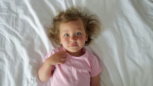 Preschooler Girl Laughs and Shows Off Foot Lying on Hotel Bed